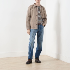 Model wearing Nudie Jeans Barney Worker Overshirt in Mud, styled with striped top, blue jeans and dark chunky shoes.