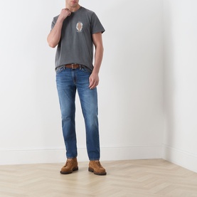 Model wearing Nudie Jeans Roy Take It Easy Logo T-Shirt in Antracite, styled with mid-blue jeans, brown leather belt and tan suede boots.