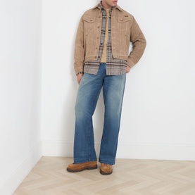 Model wearing Nudie Jeans Casual Jacket in G13 Mud, styled with plaid shirt, blue wide-leg jeans and tan boots.