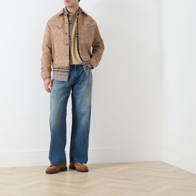 Model wearing Nudie Jeans 3049 Loose Jeans in Blue Painter, styled with a tan suede jacket, yellow top and brown loafers.