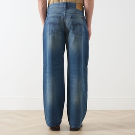 Model wearing Nudie Jeans 3049 loose jeans in Blue Painter, shown from behind with faded wash detailing and five-pocket styling.