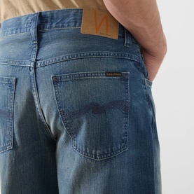 Model wearing Nudie Jeans 3049 loose fit jeans in Blue Painter, rear view showing faded denim, branded patch and five-pocket styling.