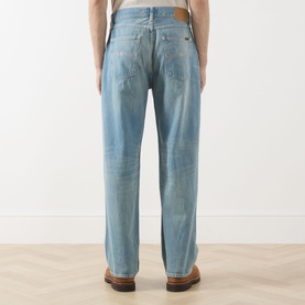 Model wearing Nudie Jeans Tuff Tony Straight Leg Jeans in Drift Wood, rear view showing faded denim, tobacco stitching and logo badge.