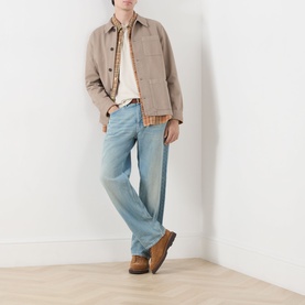 Model wearing Nudie Jeans Tuff Tony Straight Leg Jeans in Drift Wood with a beige chore jacket, plaid shirt and brown boots.