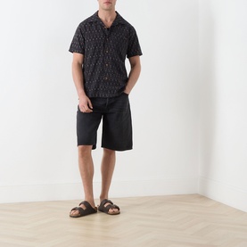 Model wearing Nudie Jeans Reg Shirt in R22 Multi dark print, styled with black shorts and tan leather sandals