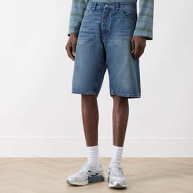 Model wearing Nudie Jeans Zeb High-Rise Wide Leg Denim Shorts in Blue Painter, wide-leg cut with faded whiskering details, styled with grey trainers.