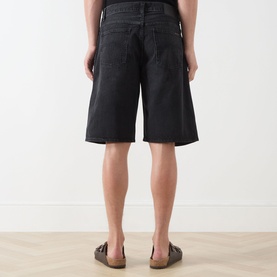 Model wearing Nudie Jeans 3049 shorts in Night Dune black denim, rear view, styled with brown sandals