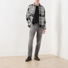 Model wearing Nudie Jeans Solid Ollie Mid-Rise Slim Leg Jeans in Pale Ash, styled with a black turtleneck, plaid overshirt and black shoes.
