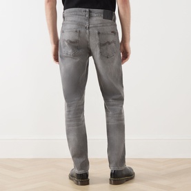 Model wearing Nudie Jeans Solid Ollie Mid-Rise Slim Leg Jeans in Pale Ash, back view, showing faded details and slim-cut legs, styled with tan shoes.