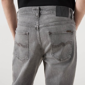 Model wearing Nudie Jeans Solid Ollie Mid-Rise Slim Leg Jeans in Pale Ash, rear view showing logo badge, whiskering and faded details.
