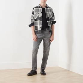 Model wearing Nudie Jeans Solid Ollie Mid-Rise Slim Leg Jeans in Pale Ash, styled with a black tee, check overshirt, and black loafers.