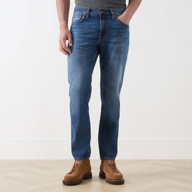 Model wearing Nudie Jeans Gritty Jackson Straight-Leg Jeans in Sun Set, mid-rise straight fit with faded whiskering details, styled with tan leather