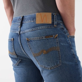 Model wearing Nudie Jeans Gritty Jackson Straight-Leg Jeans in Sun Set, showing back pockets with tobacco stitching and logo badge detail.