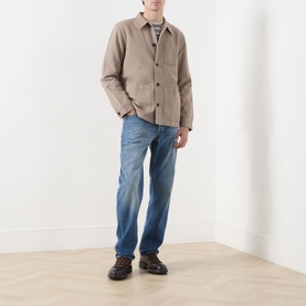 Model wearing Nudie Jeans 3049 straight jeans in Slow Drive with a stone overshirt and dark brown leather boots.