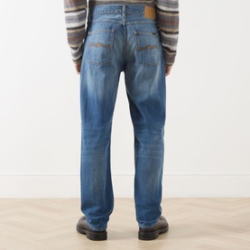 Model wearing Nudie Jeans 3049 straight jeans in Slow Drive mid-blue wash, styled with a striped jumper and dark boots.