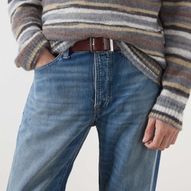 Model wearing Nudie Jeans 3049 straight jeans in Slow Drive blue with a brown leather belt and striped knit jumper.