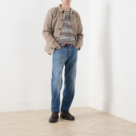 Model wearing Nudie Jeans 3049 straight jeans in Slow Drive mid-blue wash, styled with beige jacket, striped top and brown leather shoes.