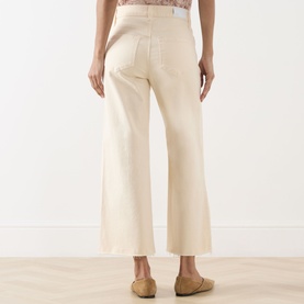 Model wearing Paige Anessa Front Pockets High-Rise Wide Leg Jeans in Butter Yellow, cropped wide leg, raw hem, rear view, styled with tan flat shoes.