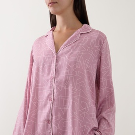 Model wearing DKNY Monogram Satin Long-Sleeved Pyjama Set in Dusty Mauve, showing notched collar, button front and long sleeves with all-over logo