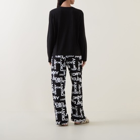 Model wearing DKNY Black Logo Plaid Pyjamas, back view, with black long-sleeve top and wide-leg logo-print trousers.