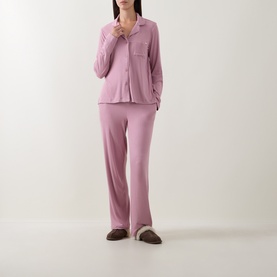 Model wearing DKNY Notched Collar Long-Sleeved Pyjama Set in Dusty Mauve, with brown slippers. Straight-leg trousers and button-front top.
