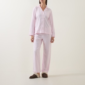 Model wearing Lauren pink print pyjamas, long-sleeve button-up top and straight-leg trousers, styled with brown fluffy slippers.