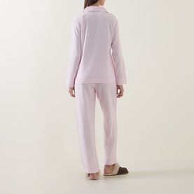 Model wearing Lauren pink printed pyjamas, long-sleeved button-front top and wide-leg trousers, rear view, with mule slippers.