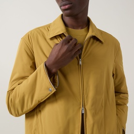 Model wearing Boss Black Casual gold casual jacket with silver zip fastening, styled with a crew-neck top underneath.