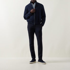Model wearing navy zip-through bomber jacket styled with matching navy trousers, light blue shirt, and grey suede trainers