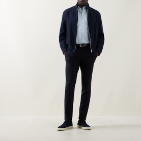 Model wearing navy bomber jacket and trousers, styled with a light blue shirt and grey slip-on trainers