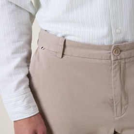 Model wearing Boss Black Casual open beige casual trousers, close-up of waistband and front pocket detail, styled with a white striped shirt.