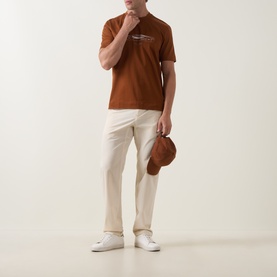 Model wearing Boss Black Casual medium brown cotton crew neck T-shirt, styled with cream trousers and white trainers, holding a tan bucket hat.