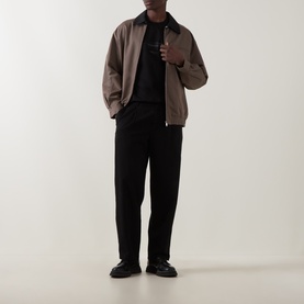 Model wearing Boss Black Casual Taut Logo T-Shirt in black, styled with a taupe zip-up jacket and black wide-leg trousers.