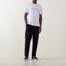 Model wearing Boss Black Casual Taut Logo T-Shirt in white with car graphic print, styled with black trousers and navy trainers.