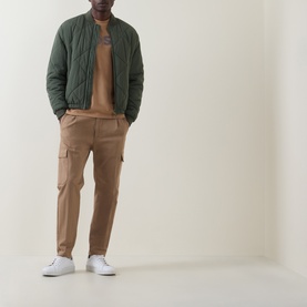 Model wearing Boss Black Casual C-Thompson Logo T-Shirt in Medium Beige, styled with green quilted bomber jacket, tan cargo trousers and white