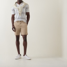 Model wearing Boss Black Casual C-Lamoroso Striped Knitted Polo in Open White, styled with beige shorts, white trainers, and a draped scarf.