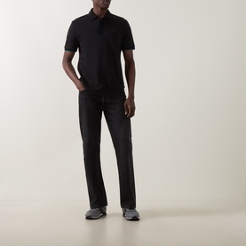 Model wearing Boss Black Casual black cotton polo shirt with short sleeves, styled with black trousers and grey trainers.