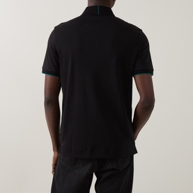 Model wearing Boss Black Casual black cotton polo shirt, back view, with green tipping on collar and cuffs, paired with dark trousers.