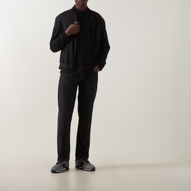 Model wearing Boss Black Casual black cotton polo, styled with black jacket, black jeans and grey trainers.