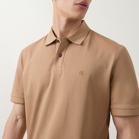 Model wearing a camel short-sleeve polo shirt with contrast buttons and small embroidered chest logo, cropped torso view