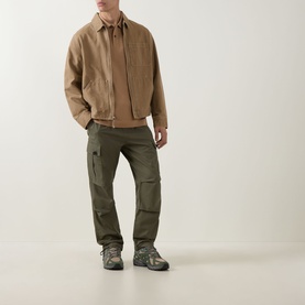 Model wearing olive green cargo trousers with multiple pockets, styled with a tan harrington jacket and grey hiking boots