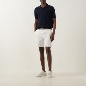 Model wearing Boss Black Casual dark blue virgin wool polo shirt, styled with white shorts, woven belt and white trainers.