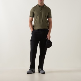 Model wearing Boss Black Casual Open Green cotton polo with tipped collar, styled with black cargo trousers and grey trainers, holding a cap.