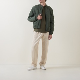 Model wearing Boss Black Casual Parlay Polo Shirt in Open Green, styled with an olive quilted bomber jacket, cream trousers and white trainers.