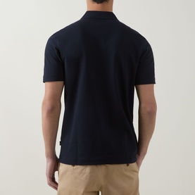 Model wearing Boss Black Casual Parlay Logo Polo Shirt in dark blue, rear view, with beige chinos. Polo collar, short sleeves, straight hem.