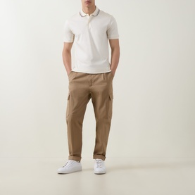Model wearing Boss Black Casual Penrose Tipped Logo Polo Shirt in Open White with stripe tipping, paired with tan cargo trousers and white trainers.