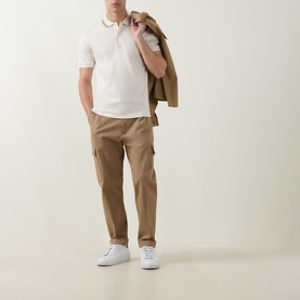 Model wearing Boss Black Casual Penrose Tipped Logo Polo Shirt in Open White with stripe tipping, styled with tan cargo trousers and white trainers.