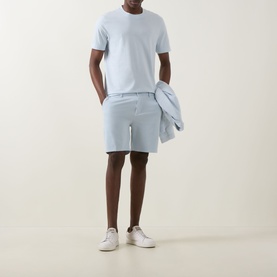 Model wearing Boss Black Casual Open Blue cotton shorts with matching shirt draped over arm, styled with light blue tee and white trainers.
