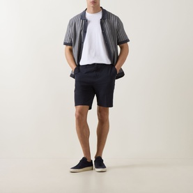 Model wearing Boss Black Casual dark blue cotton shorts with striped short-sleeve shirt and white tee, styled with navy trainers.