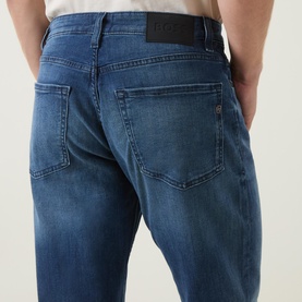 Model wearing Boss Black Casual P-Re.Maine Slim-Leg Jeans in dark blue, showing rear logo patch, five-pocket styling and mid-wash stretch denim